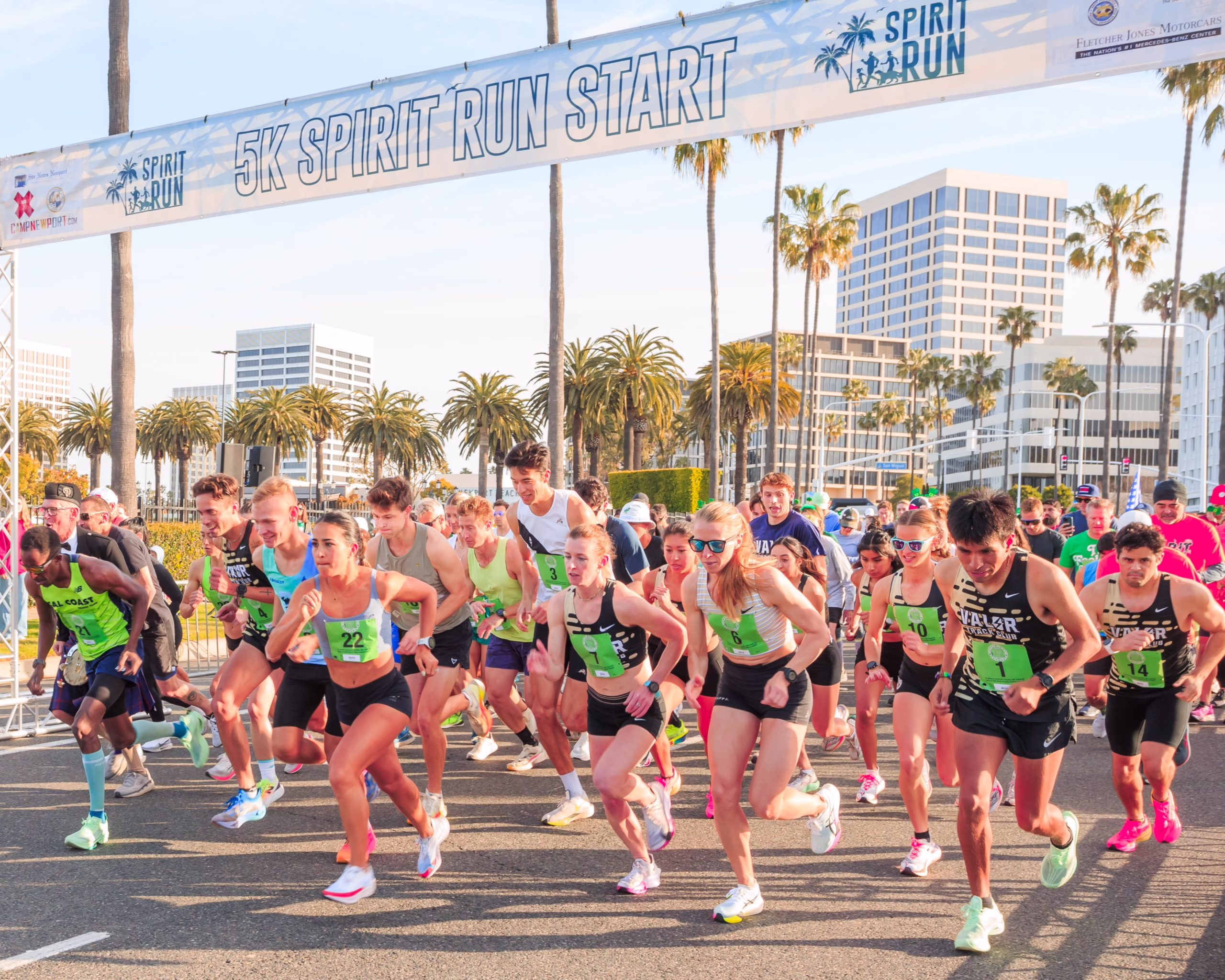 Runners begin their race with palm trees and buildings in the background
